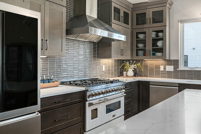 kitchen featuring tasteful backsplash, stainless steel dishwasher, wall chimney range hood, and range with two ovens