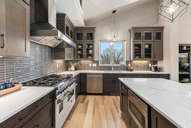 kitchen with decorative backsplash, appliances with stainless steel finishes, light wood-style floors, wall chimney exhaust hood, and a sink