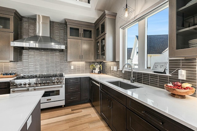 kitchen featuring light wood finished floors, a sink, stainless steel stove, wall chimney range hood, and decorative light fixtures