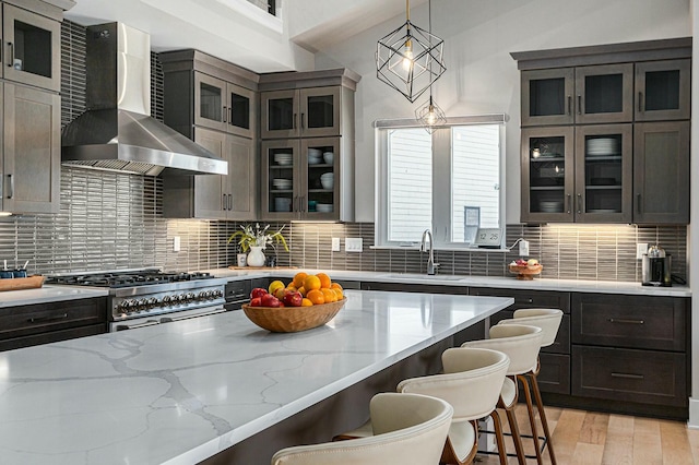 kitchen featuring a breakfast bar area, decorative backsplash, stove, wall chimney exhaust hood, and a sink