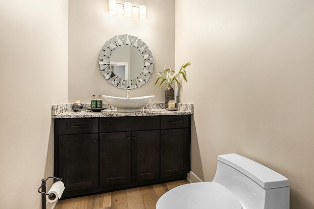 bathroom with toilet, vanity, baseboards, and wood finished floors