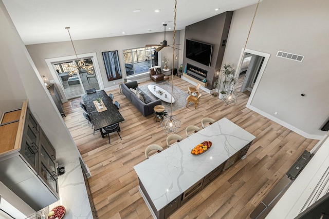 living room featuring visible vents, high vaulted ceiling, a large fireplace, light wood finished floors, and ceiling fan