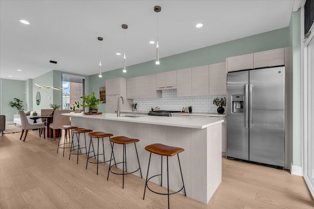 kitchen with light wood-style flooring, a sink, appliances with stainless steel finishes, a breakfast bar area, and light countertops