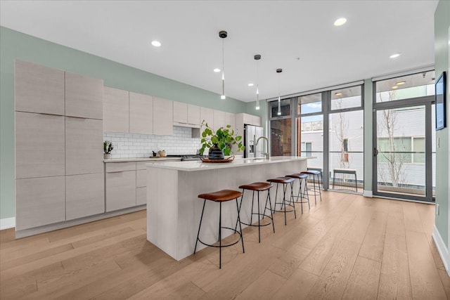 kitchen featuring decorative backsplash, stainless steel fridge, light wood-style flooring, and expansive windows