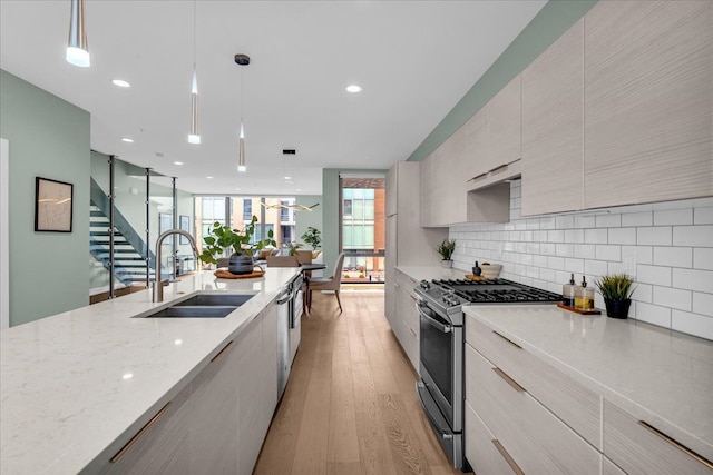 kitchen with stainless steel range with gas stovetop, a sink, light wood-style floors, modern cabinets, and backsplash