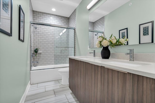 bathroom featuring double vanity, toilet, bath / shower combo with glass door, and a sink