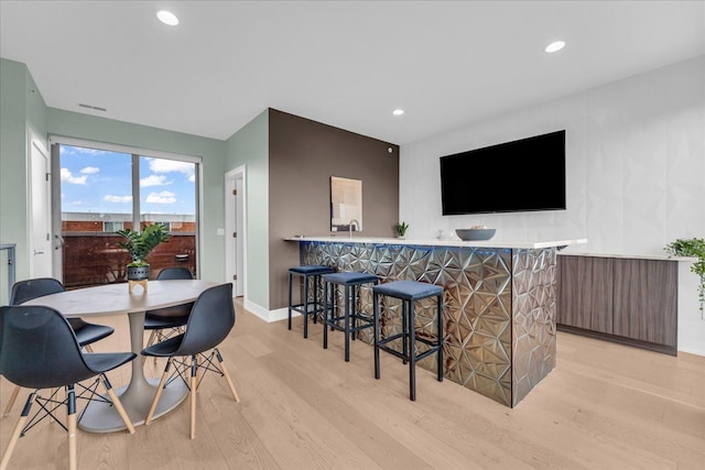 dining area featuring light wood-style flooring, bar area, recessed lighting, and baseboards