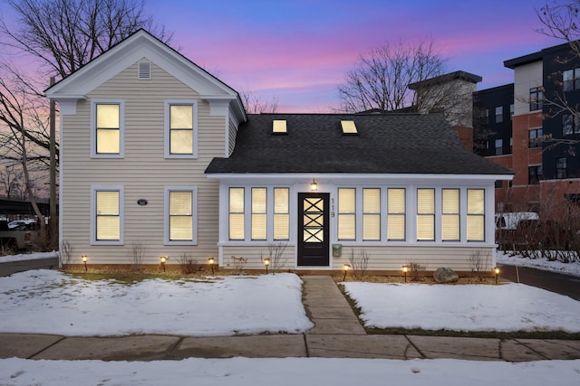 snow covered front of house with a chimney and a shingled roof