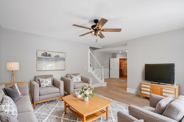 living room with stairs, baseboards, light wood finished floors, and ceiling fan