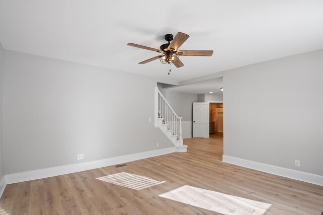 spare room with visible vents, light wood finished floors, baseboards, stairway, and a ceiling fan