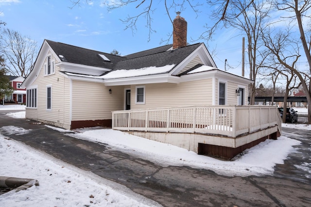 snow covered rear of property with a chimney, a deck, and roof with shingles