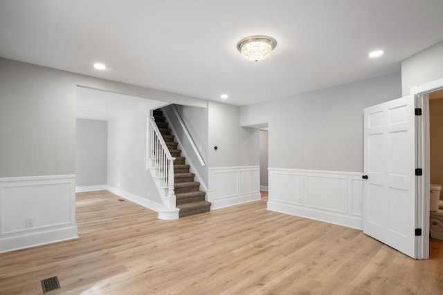 finished basement with stairway, recessed lighting, visible vents, light wood-style flooring, and wainscoting