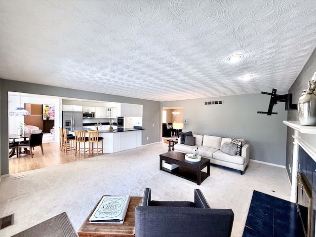 living area with a fireplace with flush hearth, light colored carpet, visible vents, and baseboards