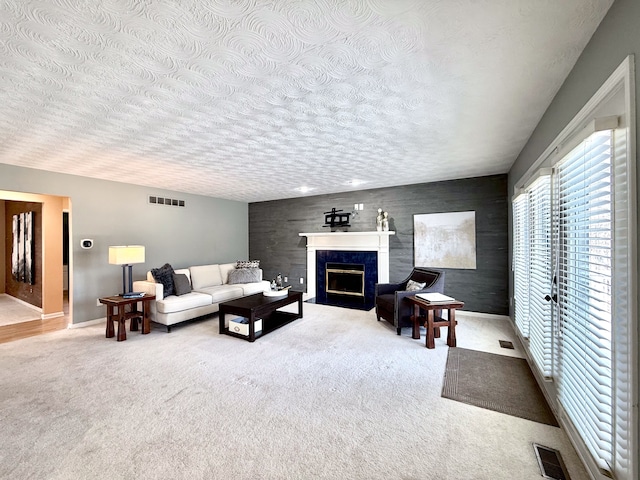 living area featuring visible vents, a textured ceiling, carpet flooring, and a high end fireplace