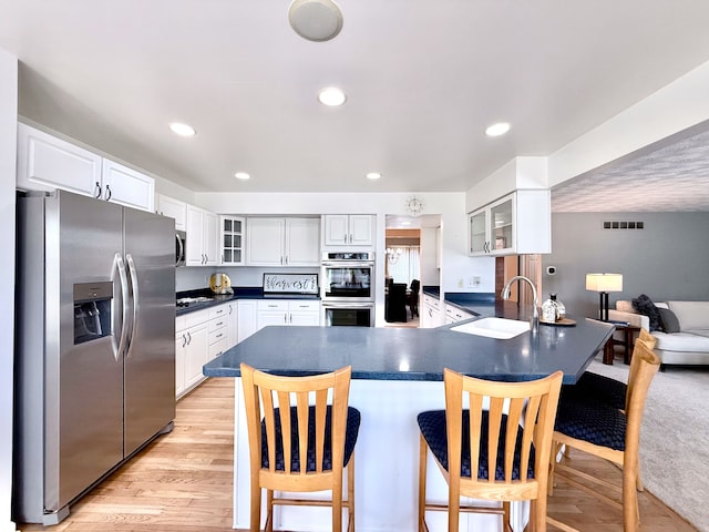 kitchen with a sink, dark countertops, appliances with stainless steel finishes, a breakfast bar area, and glass insert cabinets