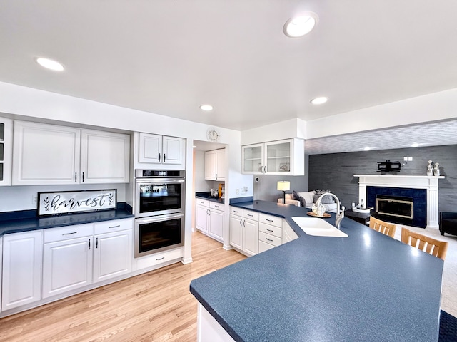 kitchen featuring light wood-style flooring, a high end fireplace, a sink, glass insert cabinets, and dark countertops