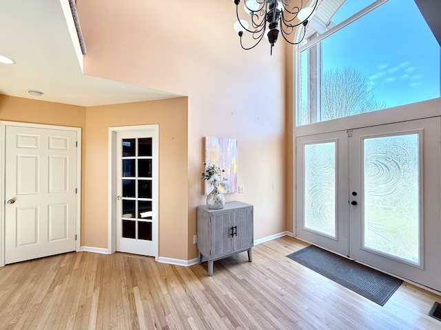 foyer with french doors, plenty of natural light, an inviting chandelier, and wood finished floors