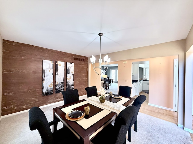 dining space featuring visible vents, an accent wall, wood walls, light colored carpet, and an inviting chandelier