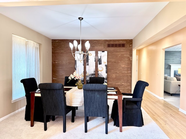 dining area with visible vents, baseboards, wood walls, wood finished floors, and a notable chandelier