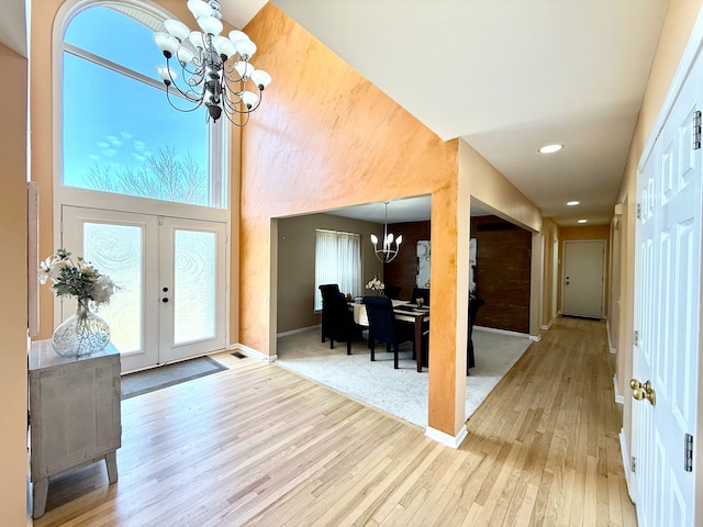 foyer featuring an inviting chandelier, plenty of natural light, light wood-style floors, and french doors