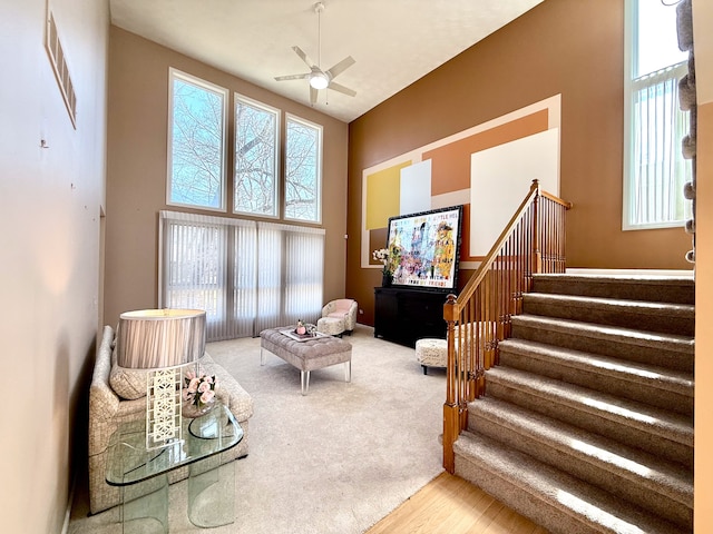 sitting room with stairway, a wealth of natural light, visible vents, and a towering ceiling