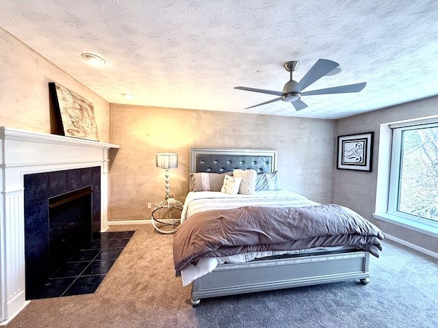 carpeted bedroom with a tiled fireplace, ceiling fan, baseboards, and a textured ceiling