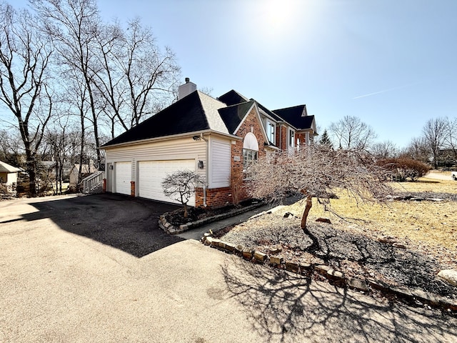 view of property exterior featuring brick siding, driveway, a chimney, and a garage