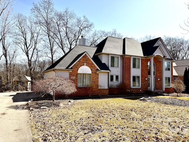 view of front of house with brick siding, driveway, and a chimney