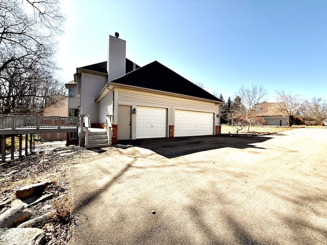 view of side of property with a deck, an attached garage, driveway, and a chimney