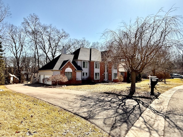 view of front of home with aphalt driveway, a garage, brick siding, and a chimney