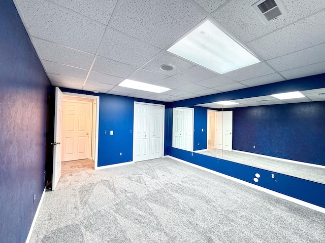 finished below grade area featuring a paneled ceiling, visible vents, baseboards, and carpet