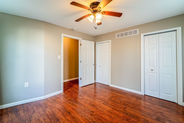 unfurnished bedroom featuring visible vents, multiple closets, wood finished floors, baseboards, and ceiling fan