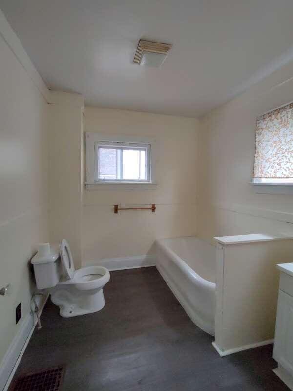 full bath with baseboards, toilet, wood finished floors, a bath, and vanity