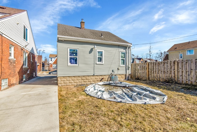 rear view of house featuring a lawn, a chimney, roof with shingles, and fence