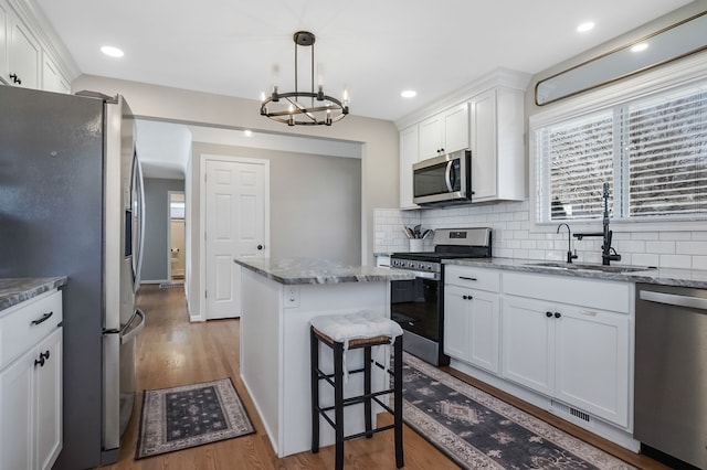 kitchen with wood finished floors, a sink, stainless steel appliances, white cabinets, and a center island