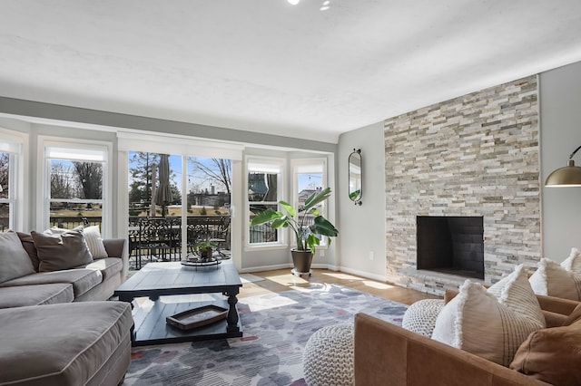 living area featuring a stone fireplace, baseboards, and wood finished floors