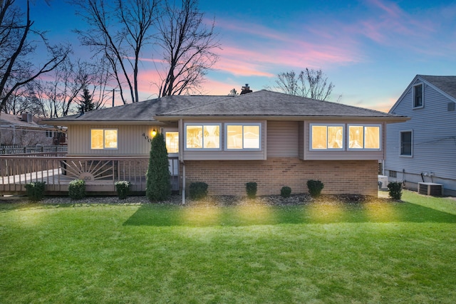 back of house at dusk featuring a deck, central AC unit, a lawn, and brick siding