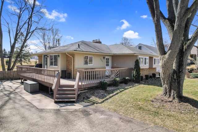 view of front of home featuring fence, a front yard, a wooden deck, brick siding, and a chimney