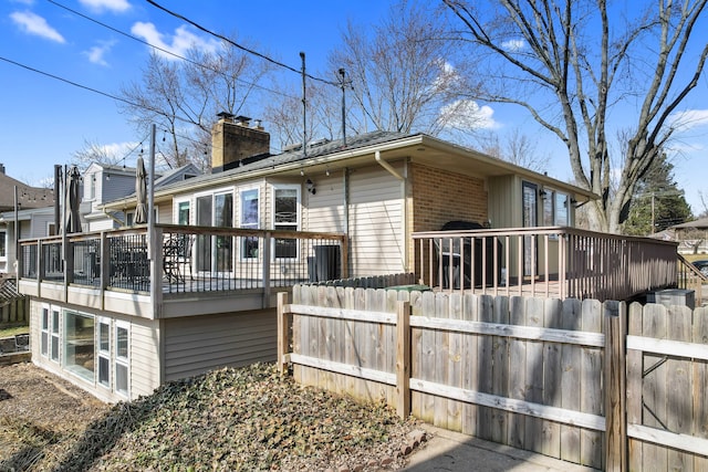 rear view of house with a deck, brick siding, a fenced front yard, and a chimney