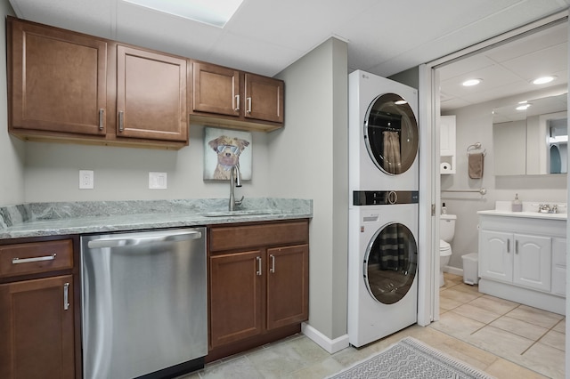 clothes washing area featuring baseboards, stacked washer and dryer, laundry area, light tile patterned flooring, and a sink