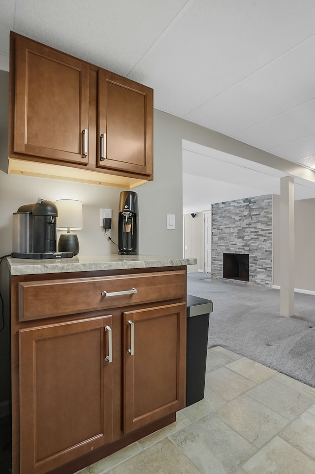 kitchen with brown cabinets, light colored carpet, a fireplace, and light countertops