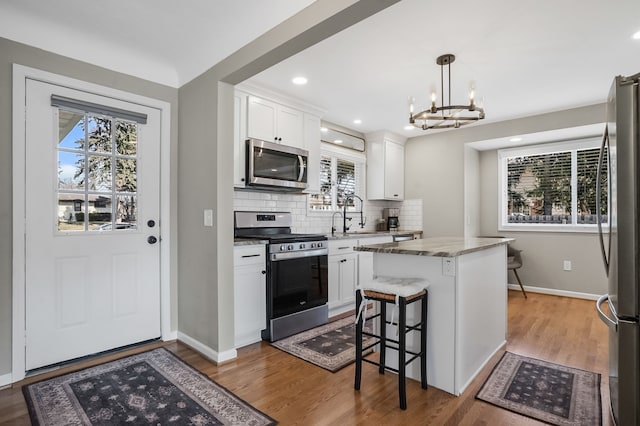 kitchen with wood finished floors, a kitchen island, a sink, appliances with stainless steel finishes, and backsplash