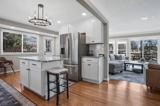 kitchen featuring backsplash, stainless steel fridge with ice dispenser, open floor plan, light wood-type flooring, and white cabinets