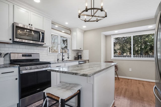 kitchen with light wood finished floors, a sink, stainless steel appliances, backsplash, and a chandelier