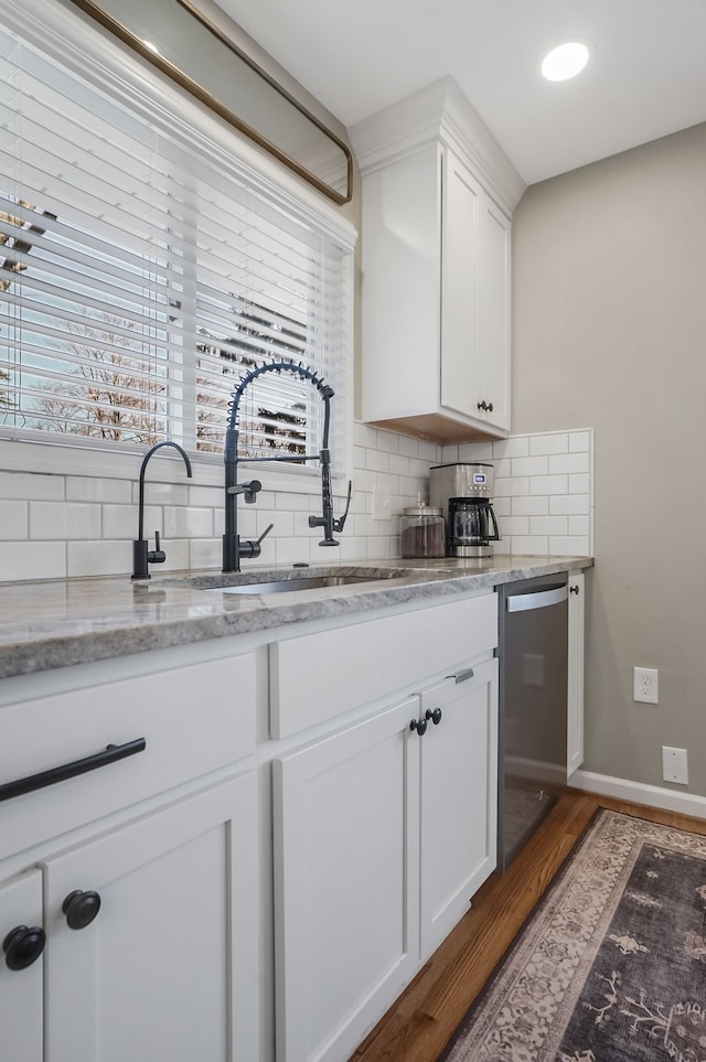 kitchen with dishwasher, decorative backsplash, wood finished floors, white cabinetry, and a sink