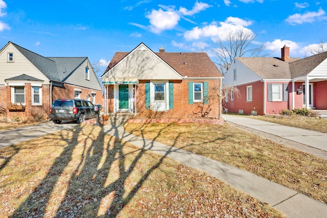 bungalow with brick siding, a front lawn, concrete driveway, roof with shingles, and a chimney