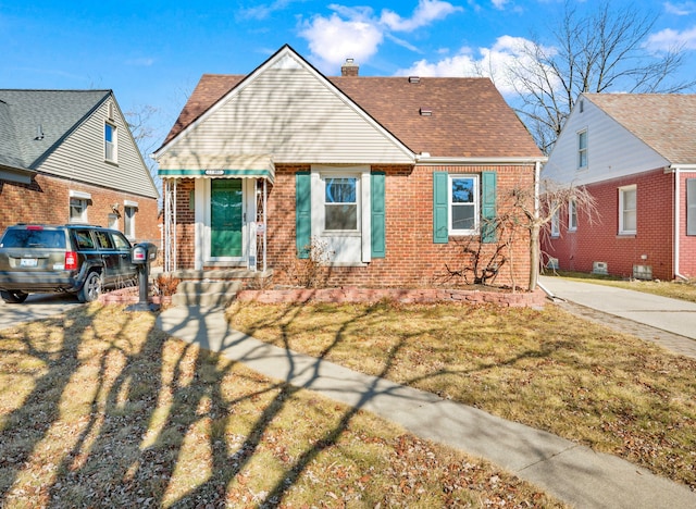 bungalow-style house with a front lawn, brick siding, a chimney, and a shingled roof