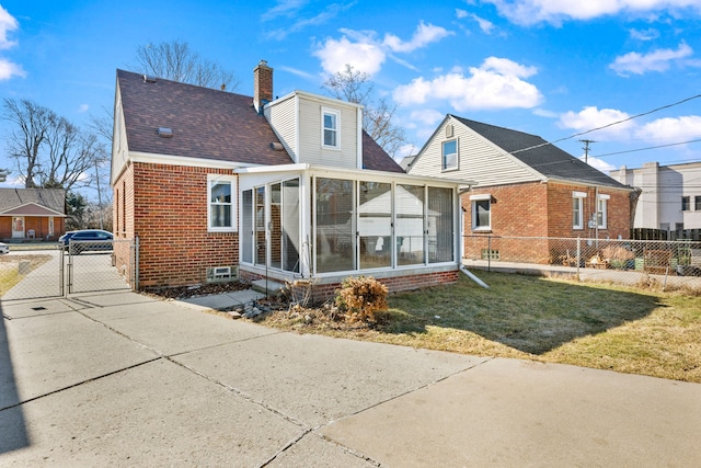 rear view of house featuring a gate, fence, a sunroom, brick siding, and a chimney