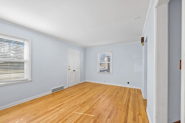 spare room with light wood-type flooring, visible vents, baseboards, and crown molding