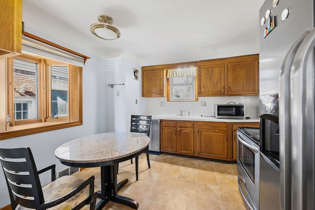 kitchen featuring brown cabinetry, a sink, stainless steel appliances, light countertops, and backsplash